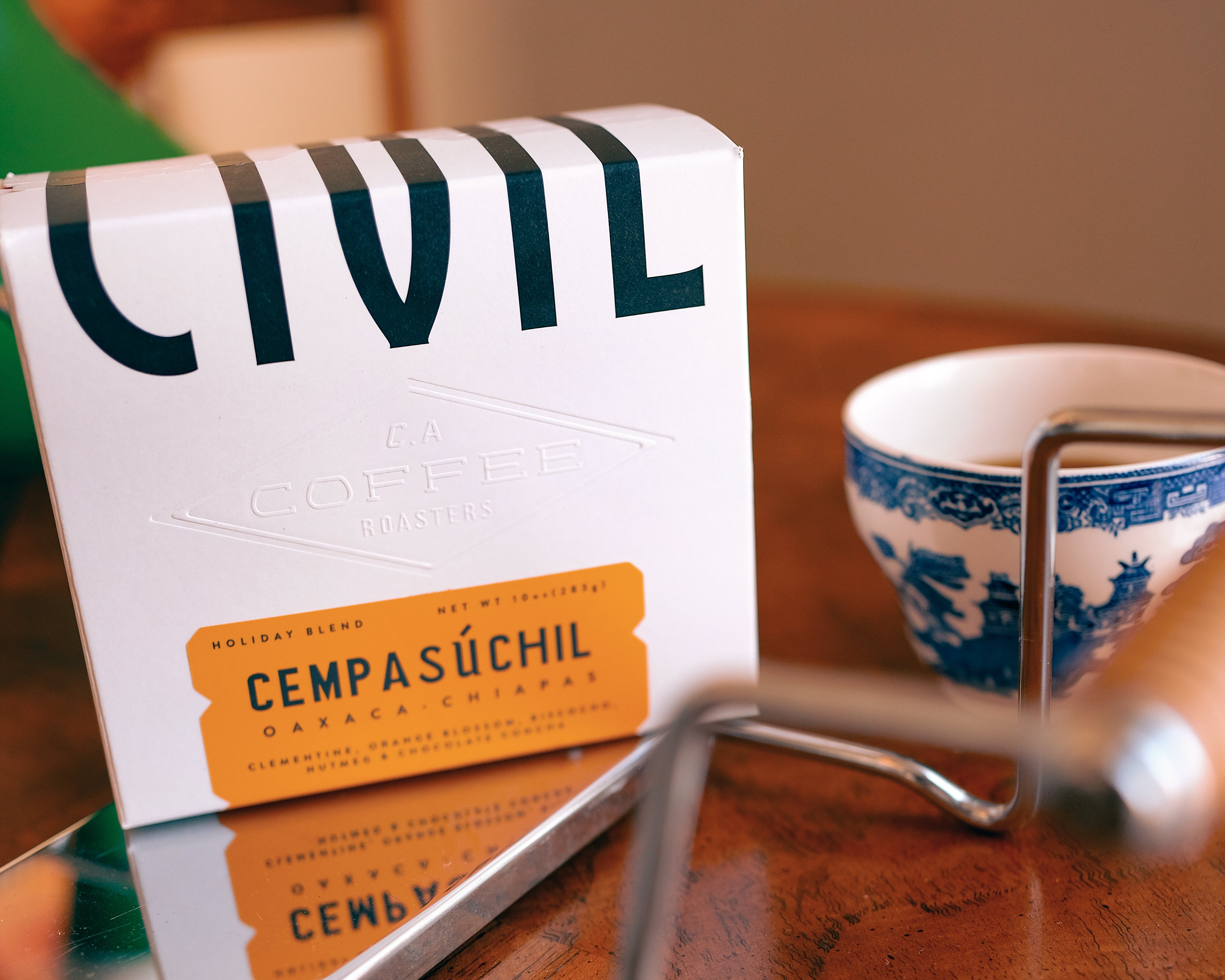 Café Civil coffee packaging on a wooden table with a coffee grinder and cup.